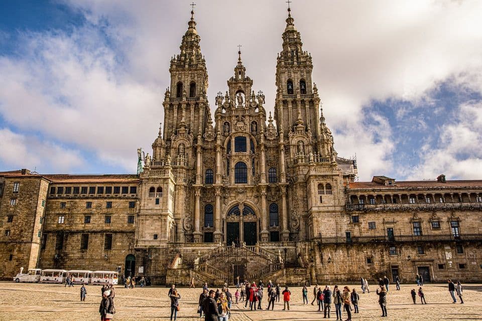 La ornamentada fachada de una gran catedral de piedra con torres gemelas domina una concurrida plaza llena de gente.