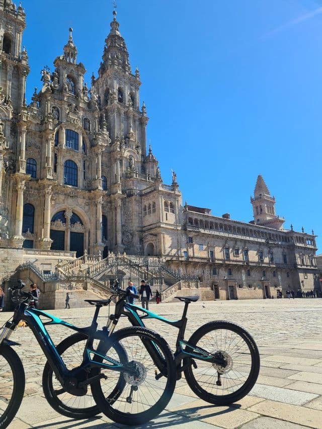 Dos bicicletas están estacionadas en una plaza empedrada frente a una catedral ornamentada bajo un cielo azul claro.