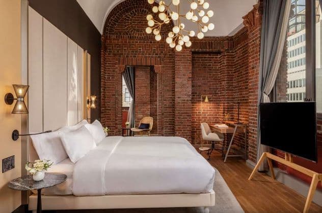 Una camera d'albergo moderna con pareti in mattoni rossi a vista, un grande letto con lenzuola bianche e un lampadario a globo contemporaneo.