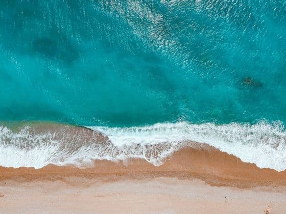 Una veduta aerea di onde turchesi con schiuma bianca che si infrangono su una spiaggia sabbiosa