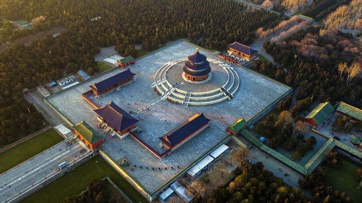 Una vista aérea de un complejo de templo tradicional chino con una pagoda circular de techo azul en una gran plaza rodeada por un denso bosque.