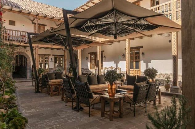 Un patio esterno con sedie a sdraio, divani e grandi ombrelloni allestito nel cortile di un edificio tradizionale.