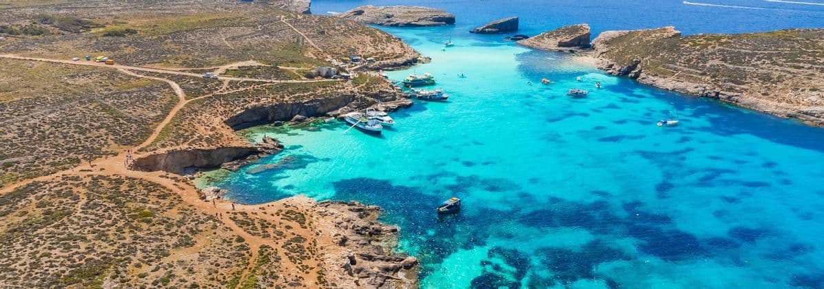 Vue aérienne d'une crique rocheuse aux eaux turquoise éclatantes, où plusieurs bateaux sont amarrés et des gens nagent.