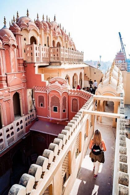 Une femme lors d'un voyage en groupe WeRoad marche sur une haute terrasse, admirant une architecture ornée de couleurs rose et pêche.