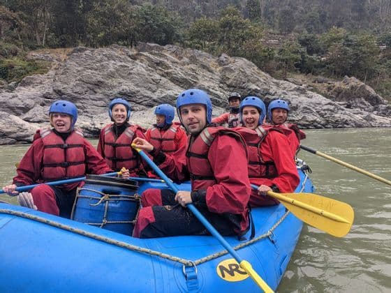 Un grupo de WeRoad, con chalecos salvavidas rojos y cascos azules, sonríe mientras hace rafting en una balsa inflable azul en un río.