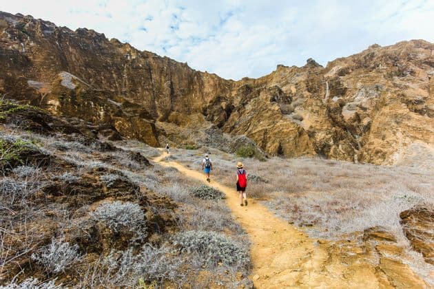 Eine WeRoad-Gruppenreise wandert auf einem schmalen Feldweg durch ein felsiges Tal, mit steilen Klippen im Hintergrund.