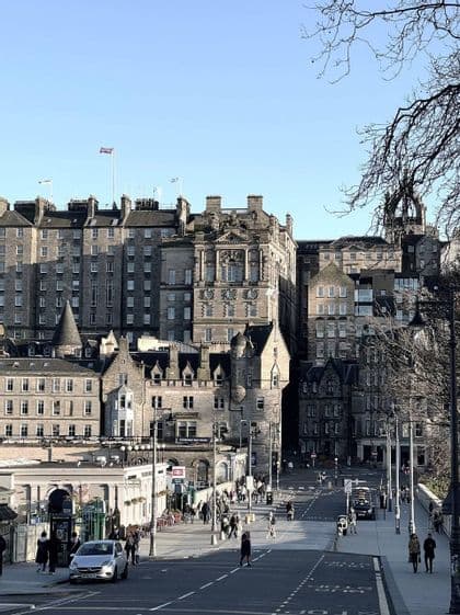 Un'assolata strada cittadina con pedoni che passeggiano lungo storici edifici in pietra sotto un cielo limpido.