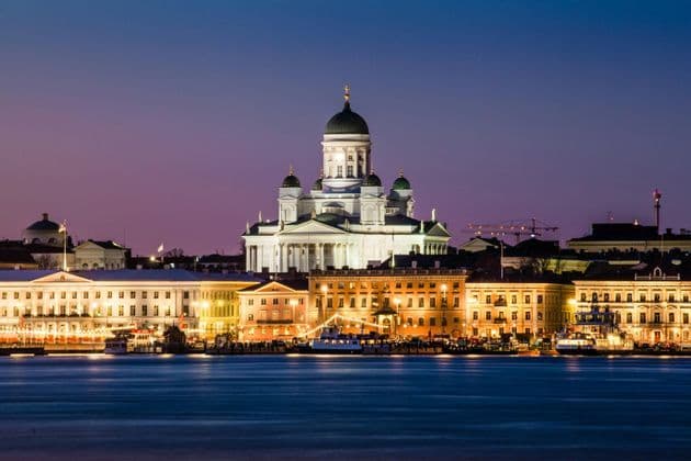 La Cattedrale illuminata di Helsinki e i palazzi sul lungomare della città, visti dall'acqua al crepuscolo.