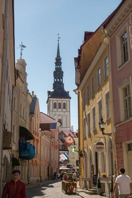 Una vista lungo una stretta strada acciottolata fiancheggiata da edifici colorati, con una grande torre di chiesa visibile sullo sfondo sotto un cielo blu.