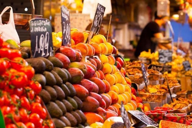 Pile colorate di pomodori freschi, avocado, manghi e pesche sono esposte in vendita su una bancarella del mercato con piccoli cartellini del prezzo.
