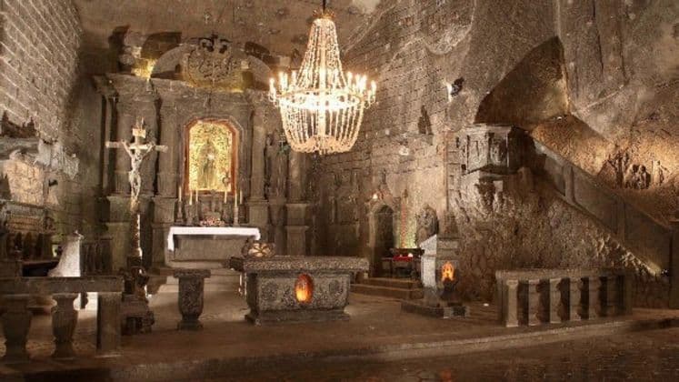 Una capilla subterránea tallada en la roca, con una gran lámpara de araña de cristal colgando sobre un altar de piedra, un crucifijo y estatuas.
