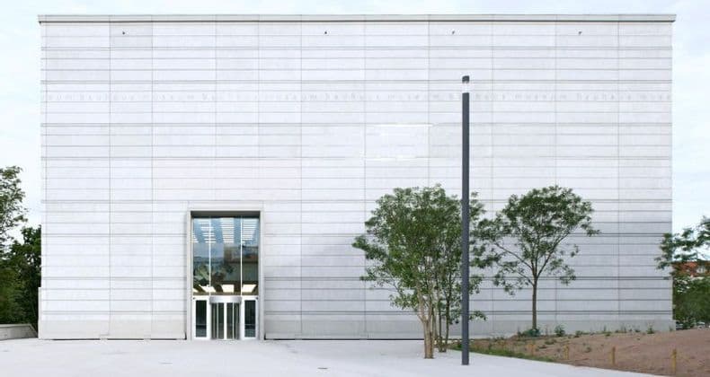 La facciata minimalista del Museo Bauhaus, con pannelli chiari, un ingresso centrale in vetro e alcuni piccoli alberi sul davanti.