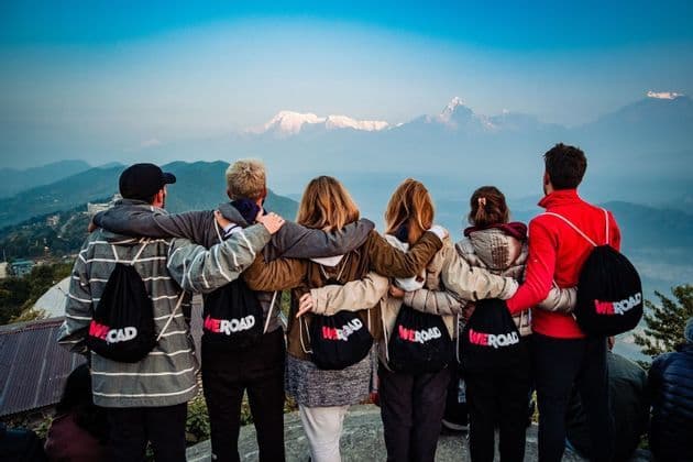 A WeRoad group trip stands with arms around each other, looking at a panoramic view of distant snow-capped mountains.