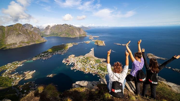 Deux personnes lors d'un voyage en groupe WeRoad, les bras levés, dominant un village côtier depuis une falaise.
