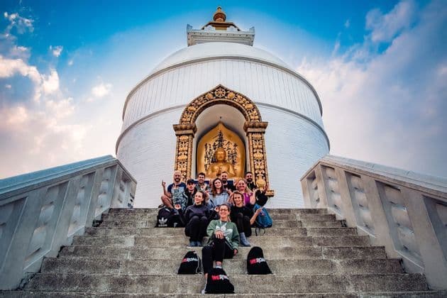 Un groupe WeRoad en voyage posant pour une photo sur les marches d'un stupa blanc avec une statue de Bouddha dorée sous un ciel bleu.