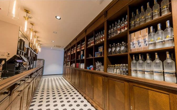 Intérieur d'un magasin d'alcool avec des étagères en bois remplies de bouteilles de vodka Ostoya et un sol carrelé géométrique.