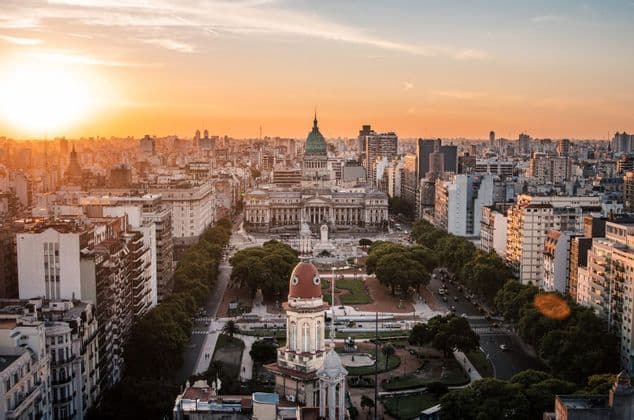 Una vista aérea de un paisaje urbano denso centrado en un gran edificio con una cúpula verde y una plaza al atardecer.
