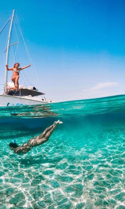 Una toma doble de un viaje en grupo de WeRoad, con una mujer en un velero y otra nadando bajo el agua en aguas claras y turquesas.