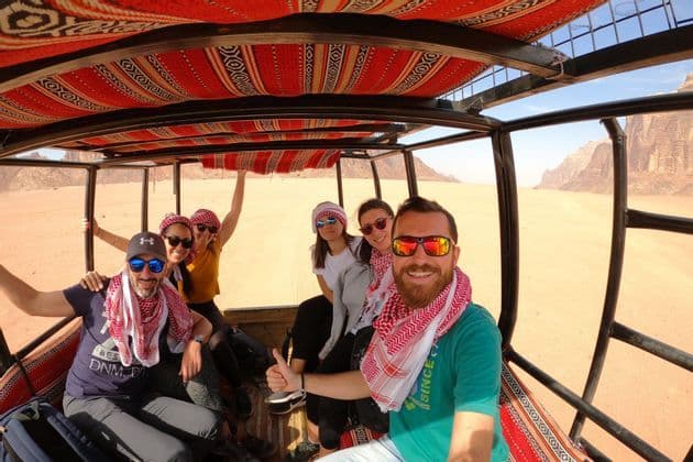 A WeRoad group trip takes a selfie in the back of an open-air vehicle while driving through a desert landscape.