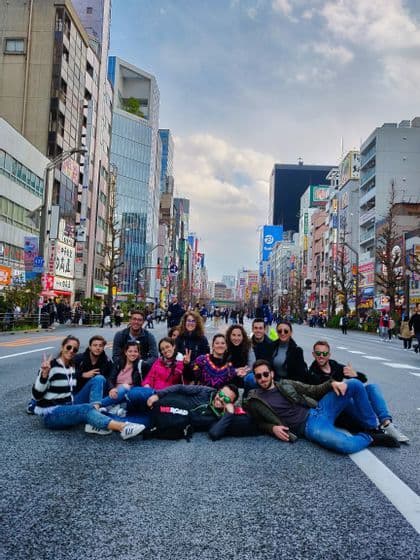 A WeRoad group trip sits together in the middle of a wide city street, posing for a photo with tall buildings in the background.
