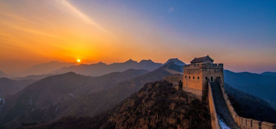 Vibranti terrazze di riso verdi su dolci colline con il sole che tramonta dietro montagne lontane sotto un cielo crepuscolare