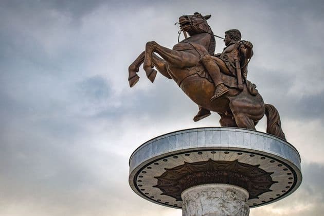 Vista dal basso di una grande statua equestre in bronzo di un guerriero su un cavallo impennato, posta su un piedistallo ornato, contro un cielo nuvoloso.