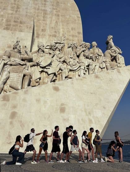 Un gruppo WeRoad in viaggio in posa in fila per imitare le statue su un grande monumento vicino all'acqua.