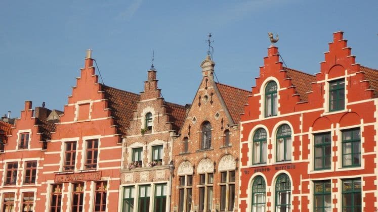 Una hilera de edificios rojos y de ladrillo con gabletes escalonados tradicionales bajo un cielo azul claro.