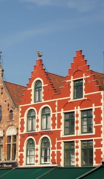 Un edificio rojo brillante con hastiales escalonados, molduras blancas y marcos de ventanas verdes se alza contra un cielo azul claro.