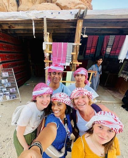 Un groupe WeRoad en voyage, portant des keffiehs assortis rouges et blancs, prend un selfie devant un stand de marché en plein air.