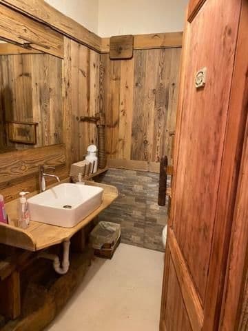 Un bagno rustico con pareti rivestite in legno di recupero, con lavabo a catino bianco su un mobile da bagno su misura in legno e una parete in pietra.