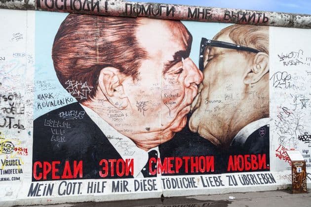 The 'Fraternal Kiss' mural by Dmitri Vrubel on the East Side Gallery section of the Berlin Wall, covered in various graffiti.