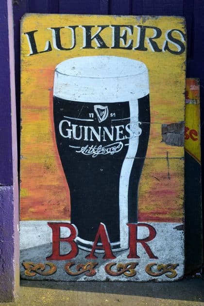 Une enseigne en bois patinée et peinte à la main pour 'Lukers Bar', représentant une grande pinte de bière Guinness sur fond jaune.