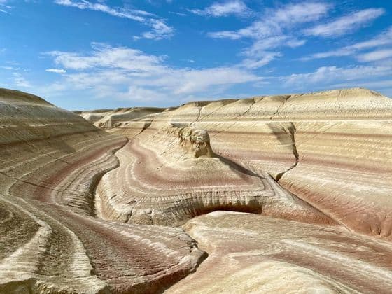 Coloridas formaciones rocosas estratificadas de sedimento rojo y blanco forman colinas ondulantes en un cañón bajo un cielo azul.