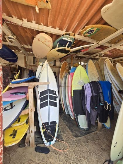 Una capanna da surf piena di numerose tavole da surf riposte verticalmente in rastrelliere e orizzontalmente sul soffitto, con mute appese nelle vicinanze.
