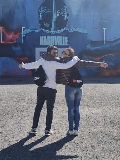Un homme et une femme d'un voyage de groupe WeRoad s'embrassent les bras tendus devant une grande fresque murale de football à Nashville.