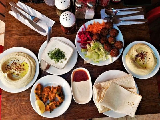 Vista cenital de una comida extendida sobre una mesa de madera, con falafel, hummus, pan de pita, ensaladas y salsas.
