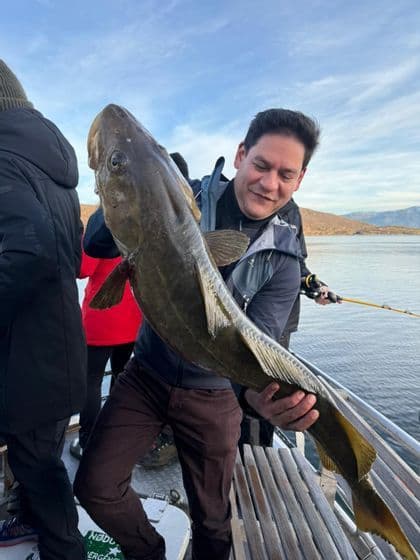 Un hombre en un viaje en grupo de WeRoad sonríe mientras sostiene un gran pez recién pescado en la cubierta de un barco.