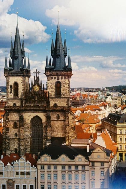 Die Zwillingstürme einer gotischen Kirche erheben sich über den roten Dächern einer historischen Stadt unter einem teils bewölkten Himmel.