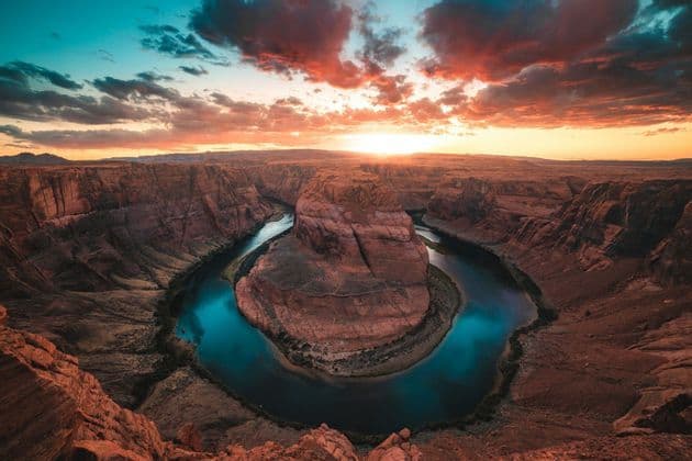 Un'ampia vista di un fiume che si snoda in un canyon di roccia rossa sotto un cielo al tramonto colorato.