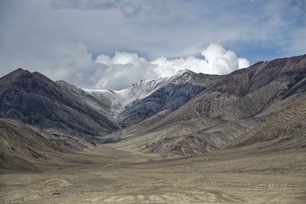 Montagne aspre e brulle con cime innevate si ergono sopra un'ampia valle arida sotto un cielo nuvoloso.