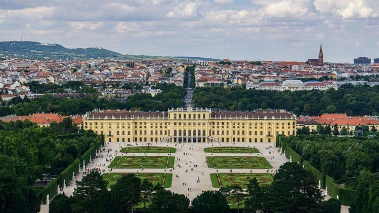 Una vista aerea di un grande palazzo giallo con i suoi ampi giardini formali, con uno skyline cittadino visibile sullo sfondo.