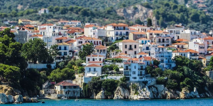 Un denso gruppo di edifici bianchi con tetti in terracotta costruiti su una lussureggiante collina verde che si affaccia su un mare blu calmo.