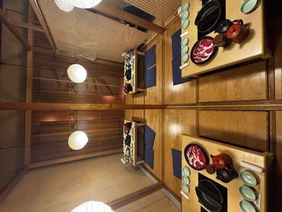 Tavoli apparecchiati per un pasto hot pot giapponese si riflettono perfettamente in un soffitto a specchio, creando una composizione completamente simmetrica.