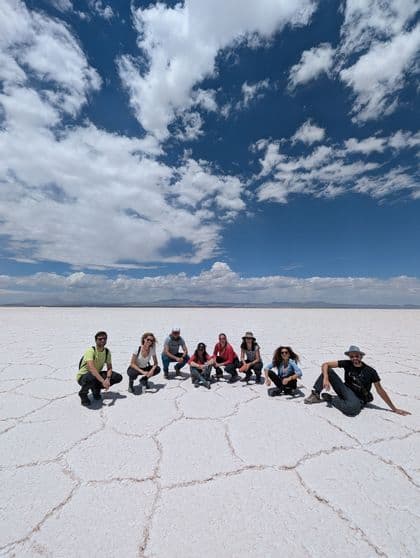 Un grupo de WeRoad posando en un extenso salar blanco bajo un cielo azul con nubes dispersas.