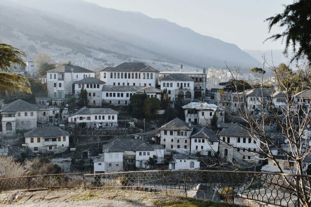 Casas de piedra blanca con techos oscuros construidas en una ladera con una gran cordillera nebulosa al fondo.