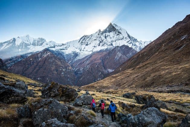 Un viaje en grupo de WeRoad haciendo senderismo por un sendero rocoso hacia una enorme montaña nevada mientras el sol sale por detrás de su cima.