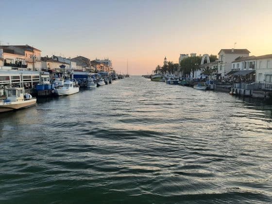Bateaux amarrés le long d'un canal bordé de bâtiments dans une ville côtière au coucher du soleil.