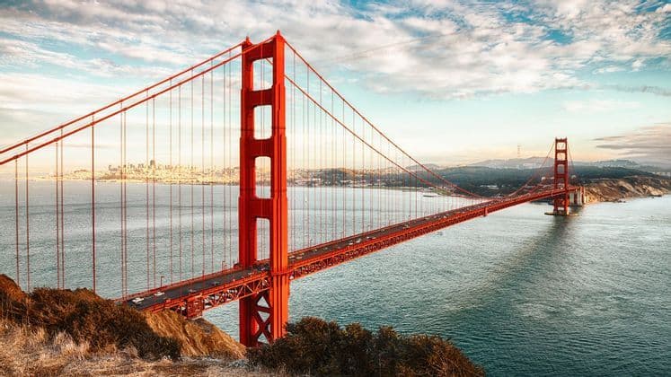 Il Ponte Golden Gate rosso che attraversa la baia all'alba, con il traffico e lo skyline della città visibile in lontananza.