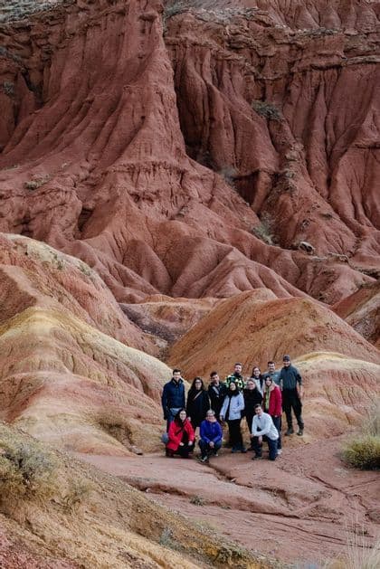 Eine WeRoad-Gruppe posiert zusammen in einer weiten Landschaft mit roten und gelben erodierten Felsformationen.